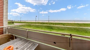 Uma varanda com vista para uma praia, área gramada e céu claro.
