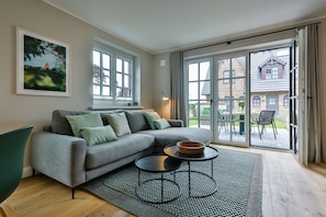 A modern living room with a grey sectional sofa, a round coffee table, and a large sliding glass door leading to an outdoor patio. - Modern new-build house with well thought-out lighting concept in a quiet location. - (Sylt)