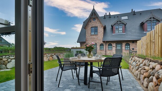 An outdoor patio with a round table and four chairs, a vase with flowers, and a stone wall.