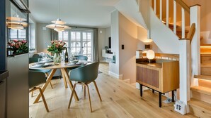 A modern kitchen with wooden flooring, a dining area with a table set for four, and a staircase with a wooden railing.