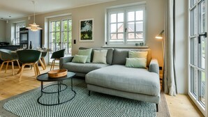 A modern living room with a grey sofa, a round coffee table, and a dining area with chairs and a table.