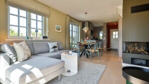 A modern living room with a grey sofa, a round coffee table, and a fireplace. - Newly built house with garden and two terraces in a salt marsh location in Tinnum. - (Sylt)