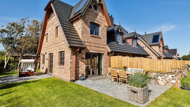A large brick house with a steeply pitched roof, a wooden deck, and a stone wall. - Newly built house with garden and two terraces in a salt marsh location in Tinnum. - (Sylt)