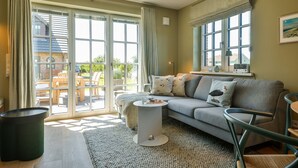 A cozy living room with a grey sofa, a small round coffee table, and a view of the outdoors through large sliding glass doors. - Newly built house with garden and two terraces in a salt marsh location in Tinnum. - (Sylt)