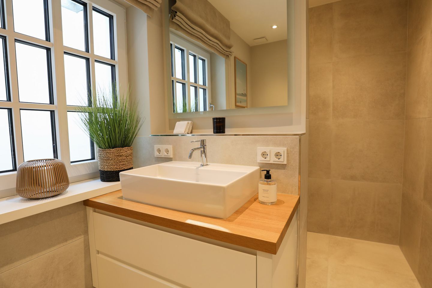 A modern bathroom with a large rectangular sink, a potted plant, and a mirror above the sink.