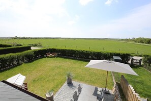 A backyard with a lawn, a wooden bench, a table with chairs, and a large umbrella. - Exclusive new-build house for 4 people in a popular salt marsh location in Tinnum. (Sylt)
