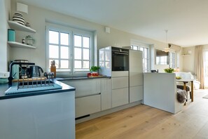 A modern kitchen with white cabinetry, a built-in oven, and a coffee machine. - Exclusive new-build house for 4 people in a popular salt marsh location in Tinnum. (Sylt)