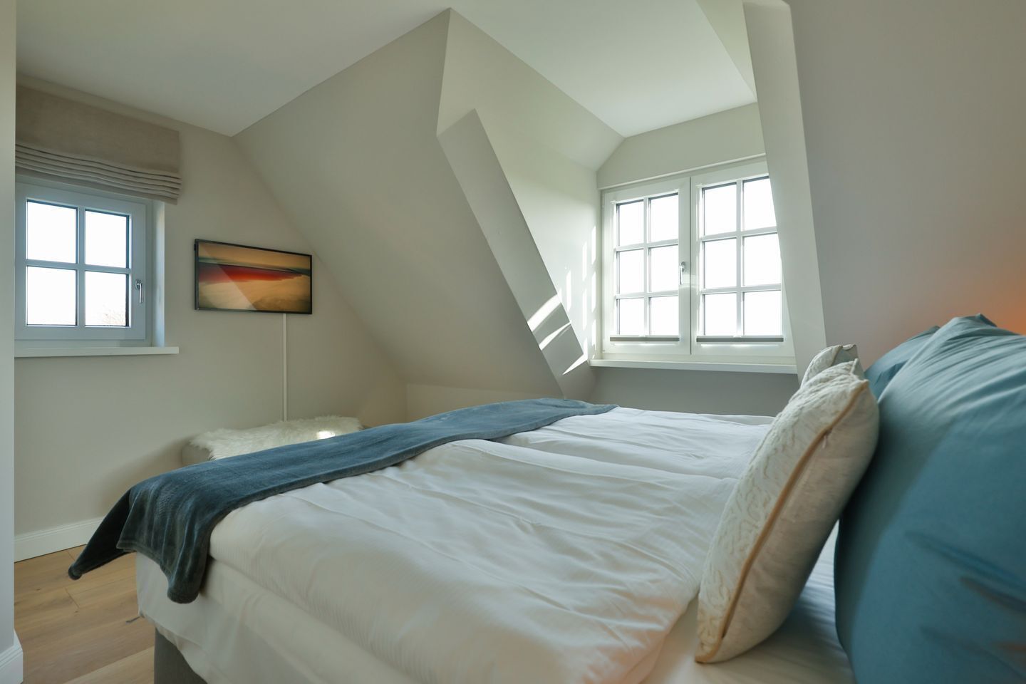 A bedroom with a bed, a window, and a painting on the wall.