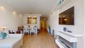 Una sala de estar moderna con un sofá blanco, una mesa de comedor con sillas, una chimenea y un televisor montado en la pared.