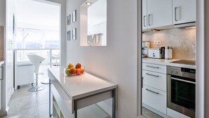 A modern kitchen with white cabinets, a built-in oven, and a countertop with a fruit bowl.