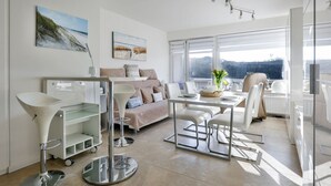 A modern living room with a sofa, dining table, and a large window offering a view of the outdoors.