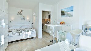 A modern bedroom with a bed, bedside table, and a view into the kitchen.
