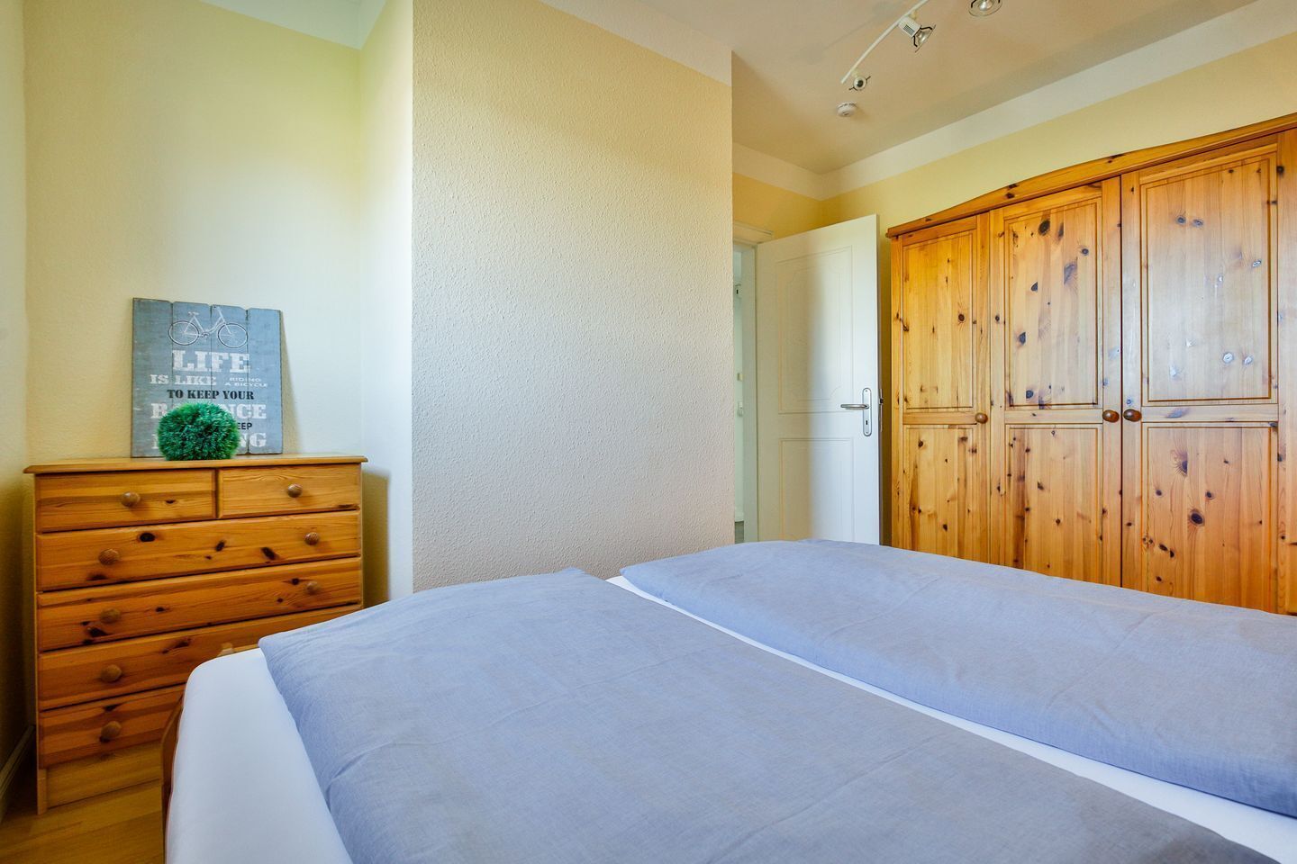 Quarto com cama, cómoda de madeira e guarda-roupa.