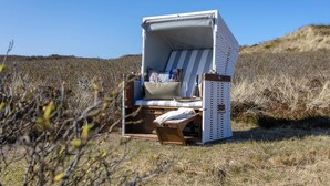 Une chaise de plage dotée d’un auvent, de coussins et d’un plateau avec un verre et une bouteille.