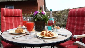 Una mesa redonda con una silla a rayas rojas, una botella, un vaso de bebida roja, un croissant y un plato de comida.