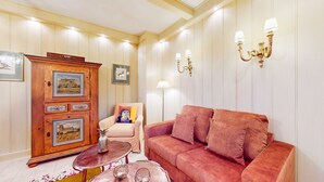 Una sala de estar con un sofá rojo, un aparador de madera con fotografías enmarcadas, una mesita redonda y una silla con un cojín de colores.
