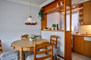 A dining area with a wooden table and chairs, a hanging light fixture, and a kitchen area with wooden cabinets and a sink.