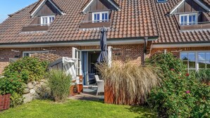 Une maison à deux étages, avec un toit en tuiles, une façade en briques et une porte d’entrée donnant sur un patio abrité.