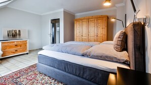 Un dormitorio con cama, armario de madera, mesita de noche, lámpara y televisión sobre un aparador.