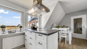 Cozinha moderna com armários brancos, ilha integrada e uma janela grande com vista para o exterior.