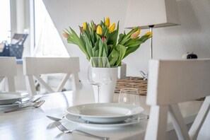 Mesa de jantar posta com pratos, talheres e um vaso de tulipas.
