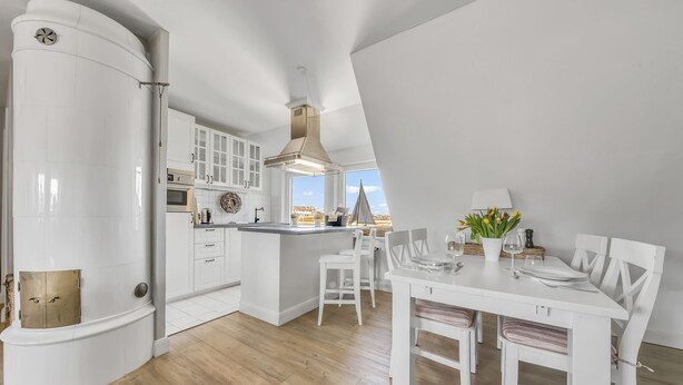 Cozinha moderna com armários brancos, uma ilha central e um espaço de refeições com mesa e cadeiras brancas.