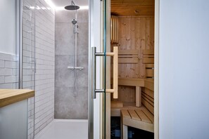 Un baño moderno con cabina de ducha de vidrio, sauna de madera y un banco de madera.