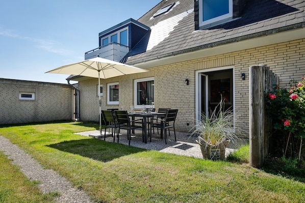 Un immeuble résidentiel doté d’un patio, d’une table à manger avec des chaises et d’un petit jardin agrémenté d’une plante en pot.