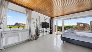 A modern bedroom with a large bed, a TV, and a view of the outdoors. - Fischer - Praktisches Appartement in Strandnaher Lage Inmitten Einer Heidelandschaft (Hörnum (Sylt))