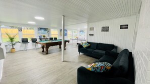 A room with a pool table, a sofa with colorful cushions, and a ping pong table.