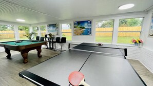 A pool table with a ping pong table, chairs, and a painting of a beach scene.