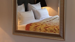 A neatly made bed with white bedding and a floral-patterned duvet, a black headboard, and a wall-mounted mirror with a decorative frame. - Spacious vacation apartment in a central location with garden and covered terrace. (Sylt)