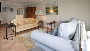 A living room with a beige sofa, a grey sofa, two small round tables, a lamp, and two paintings on the wall. - Spacious vacation apartment in a central location with garden and covered terrace. (Sylt)