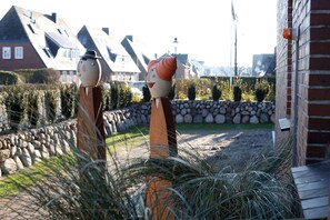 Ein Garten mit zwei Skulpturen, einer Steinsäule und einem Gebäude mit Satteldach.