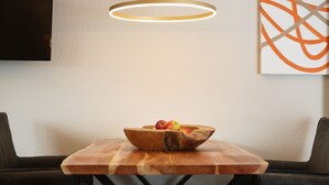 Taula de dinar amb un bol de fusta ple de fruita, una làmpada penjant moderna i una obra d'art minimalista a la paret.