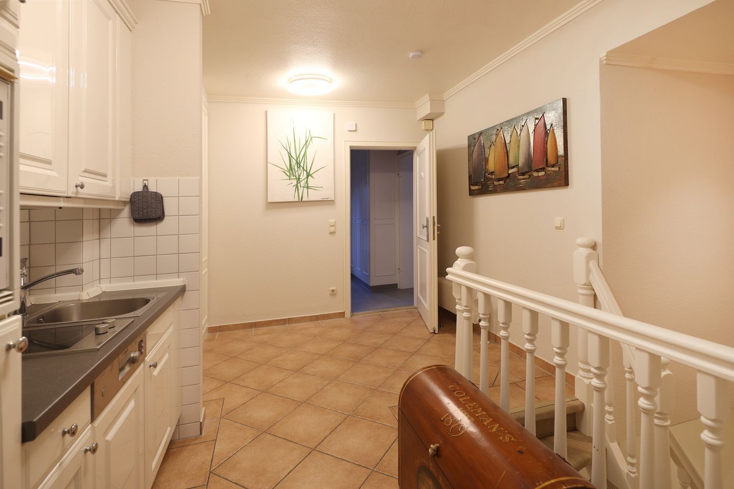 A kitchen with a sink, cabinets, and a staircase leading to another room.
