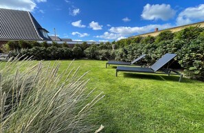 Jardín trasero con césped, dos sillones de descanso y un panel solar.