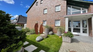 A two-story brick house with a front porch, a small garden with rocks and plants, and a clear blue sky. - Bright vacation apartment in a central location close to the beach in Westerland. - Beach villa (Sylt)