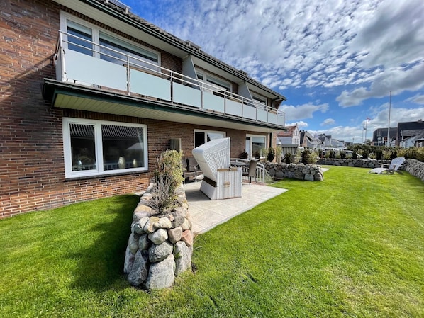 A two-story house with a balcony, a stone wall, and a well-maintained lawn.