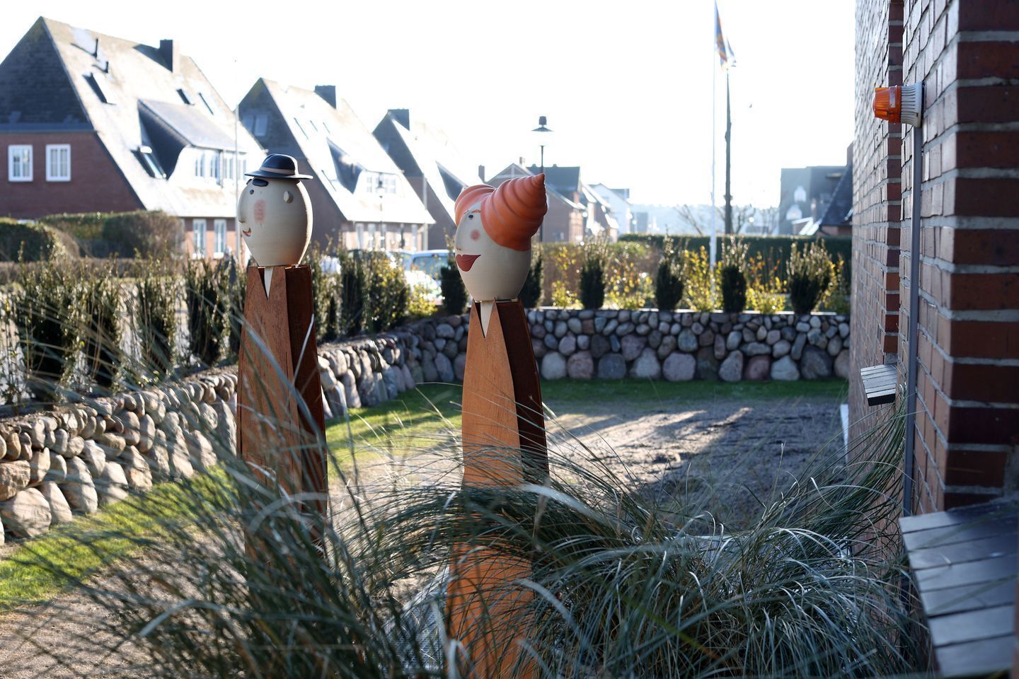 Un jardin agrémenté de deux sculptures, d’un mur en pierre et d’un bâtiment doté d’un toit en pente.