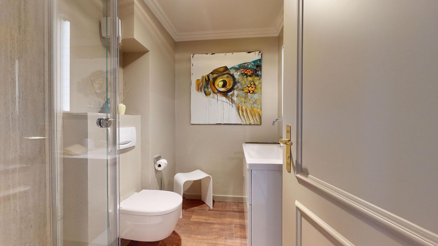 A compact bathroom with a toilet, a small sink, and a glass shower enclosure.
