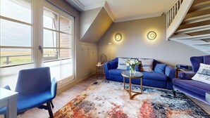Una sala de estar con un sofá azul, una mesa de centro y vistas al exterior a través de ventanas amplias.