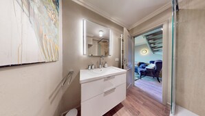 Un baño moderno con un espejo grande, tocador blanco y zona de ducha visible a través de una puerta abierta.