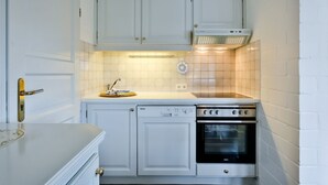 Cocina compacta con armarios blancos, lavavajillas, horno y microondas integrado.