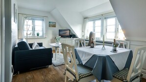 Un comedor acogedor con una mesa lista para dos, un televisor sobre un mueble y una ventana con cortinas.