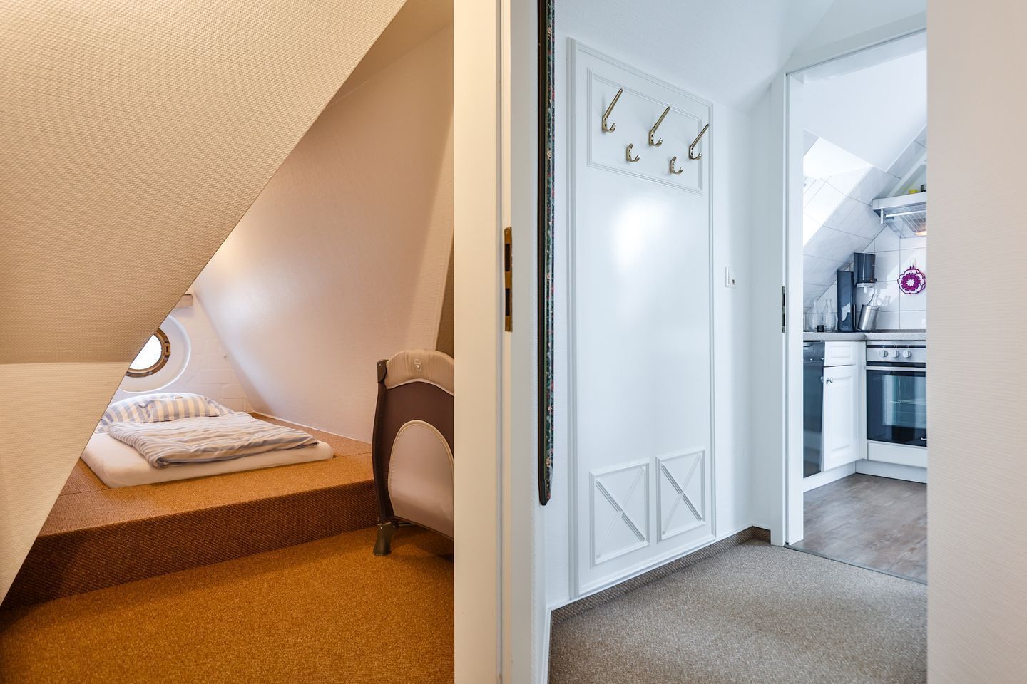 A bedroom with a sloped ceiling, a bed, a chair, and a door with hooks.