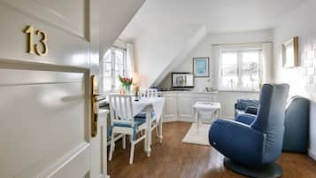 Una habitación moderna y bien iluminada con comedor, una sala de estar con sillas azules y una cocina con gabinetes blancos.