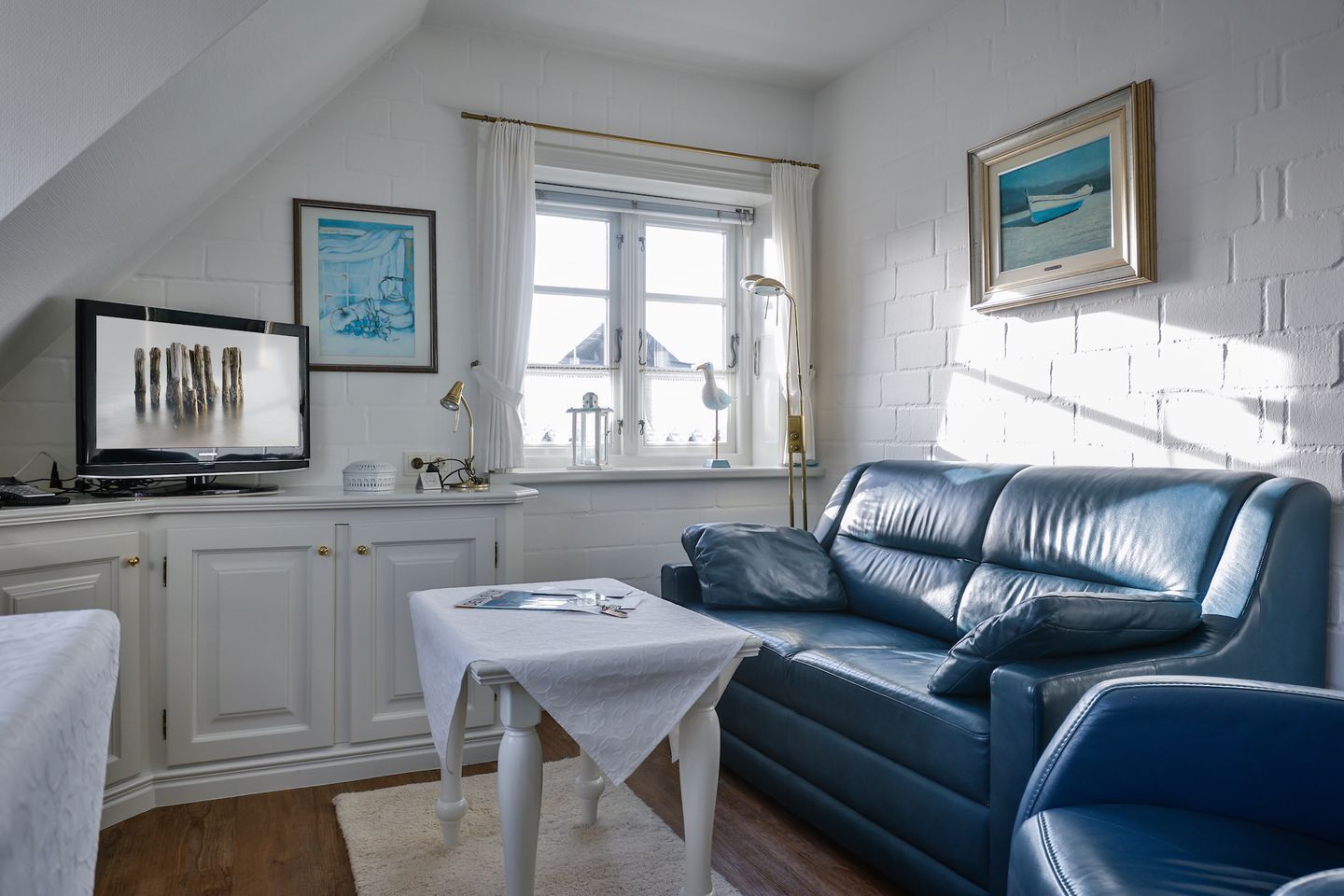 Une pièce confortable avec un canapé en cuir bleu, une petite table, un téléviseur et une fenêtre avec des rideaux.