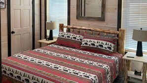 Een slaapkamer met een houten plafond, een bed met een beddengoed met een patroon, twee nachtkastjes met lampen, en een deur.