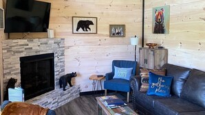Een knusse woonkamer met een open haard, een plafondventilator, een televisie en een berenthema.